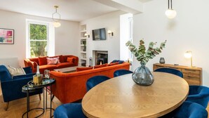 A modern living room with a wooden dining table surrounded by blue chairs, a fireplace, and a large window. - Kirkton Family Farmhouse With Hot Tub Alford Aberdeenshire (Alford)