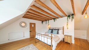 A bedroom with a sloped ceiling, wooden beams, a bed with a metal frame, bedside tables, and a radiator. - Kirkton Family Farmhouse With Hot Tub Alford Aberdeenshire (Alford)