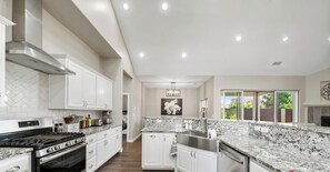 Une cuisine moderne avec des meubles blancs, des comptoirs en granit, une hotte de cuisinière en acier inoxydable et une grande fenêtre.