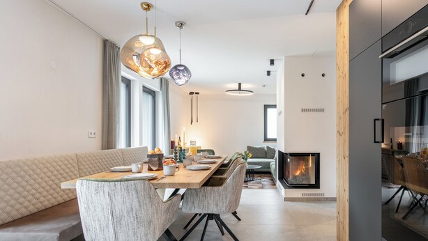 Un comedor moderno con una mesa de madera, asientos acolchados e iluminación colgante.