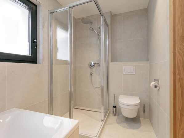 Un baño moderno con ducha de vidrio, inodoro blanco y bañera.