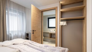 Un dormitorio moderno con una cama grande, un armario de madera, un espejo y un baño visible a través de una puerta abierta.