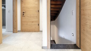 Un pasillo con una puerta de madera, una escalera y piso de baldosas.