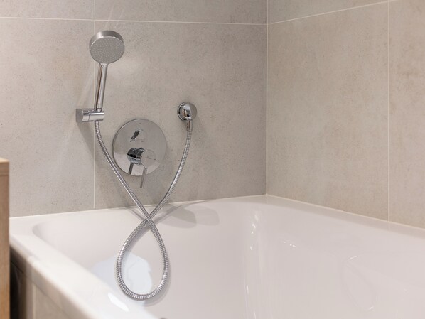 A modern bathroom with a bathtub, a handheld showerhead, and a wall-mounted control panel.