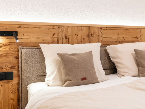 Una cama bien hecha con cabecera, una pared con textura y un objeto negro pequeño en la pared.