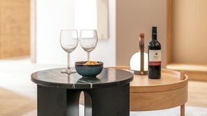 A modern room with a round table holding two wine glasses and a bowl of nuts, a bottle of wine, and a lamp.