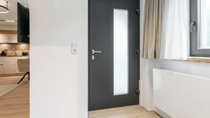 A modern kitchen with a dark door, a window with curtains, and a light-colored floor.