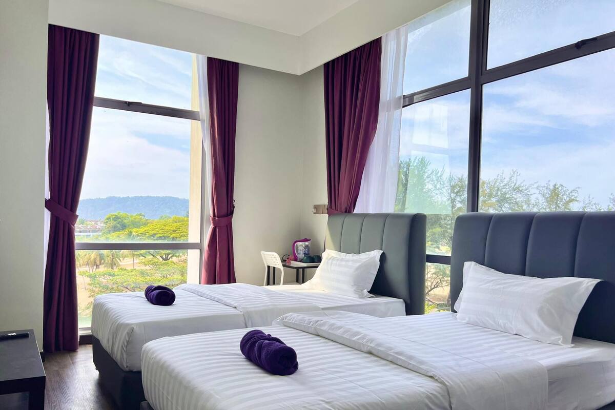 Une chambre d’hôtel avec deux lits, de grandes fenêtres et une vue sur l’extérieur.