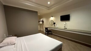 Habitación de hotel con cama, una silla, televisor, espejo y perchero.