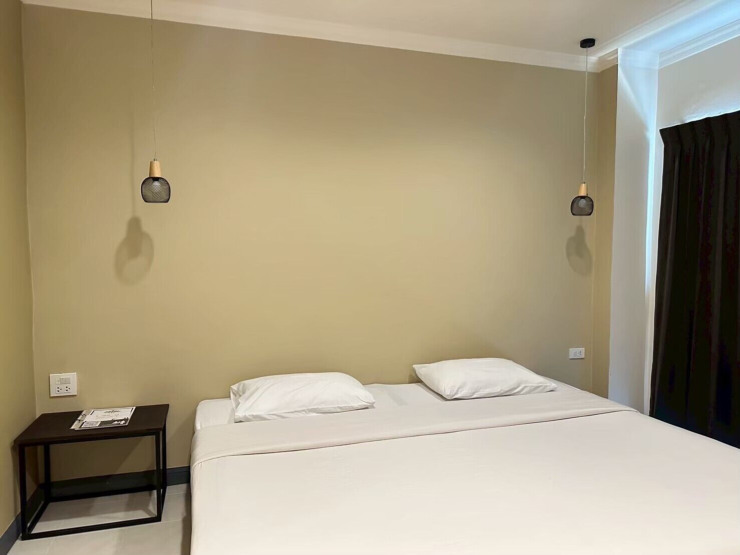 Una habitación de hotel con una cama, una mesita de noche y dos lámparas fijadas a la pared.