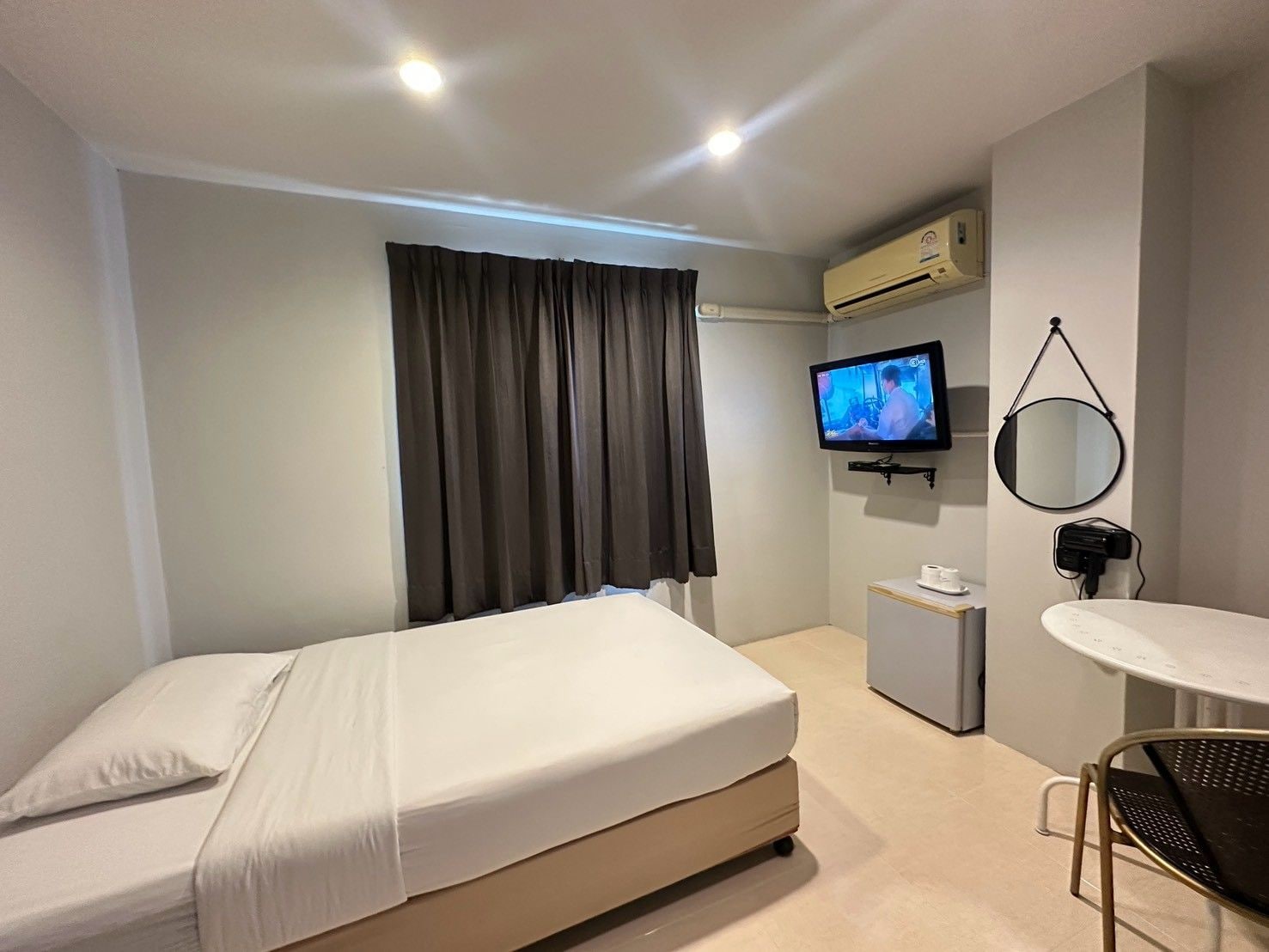 A hotel room with a bed, a TV, a small table, and a mirror.