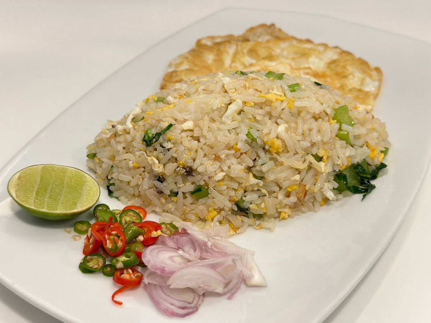 Un plato de arroz frito con verduras y huevo, acompañado de lima, jalapeños en rodajas y cebolla roja.