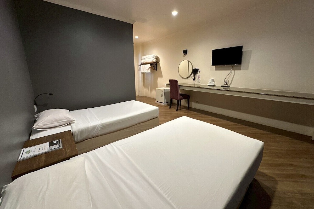 A hotel room with two single beds, a desk, a chair, a TV, and a mirror.