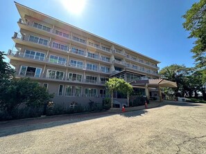 A multi-story hotel with balconies, a covered entrance, and a gravel driveway.