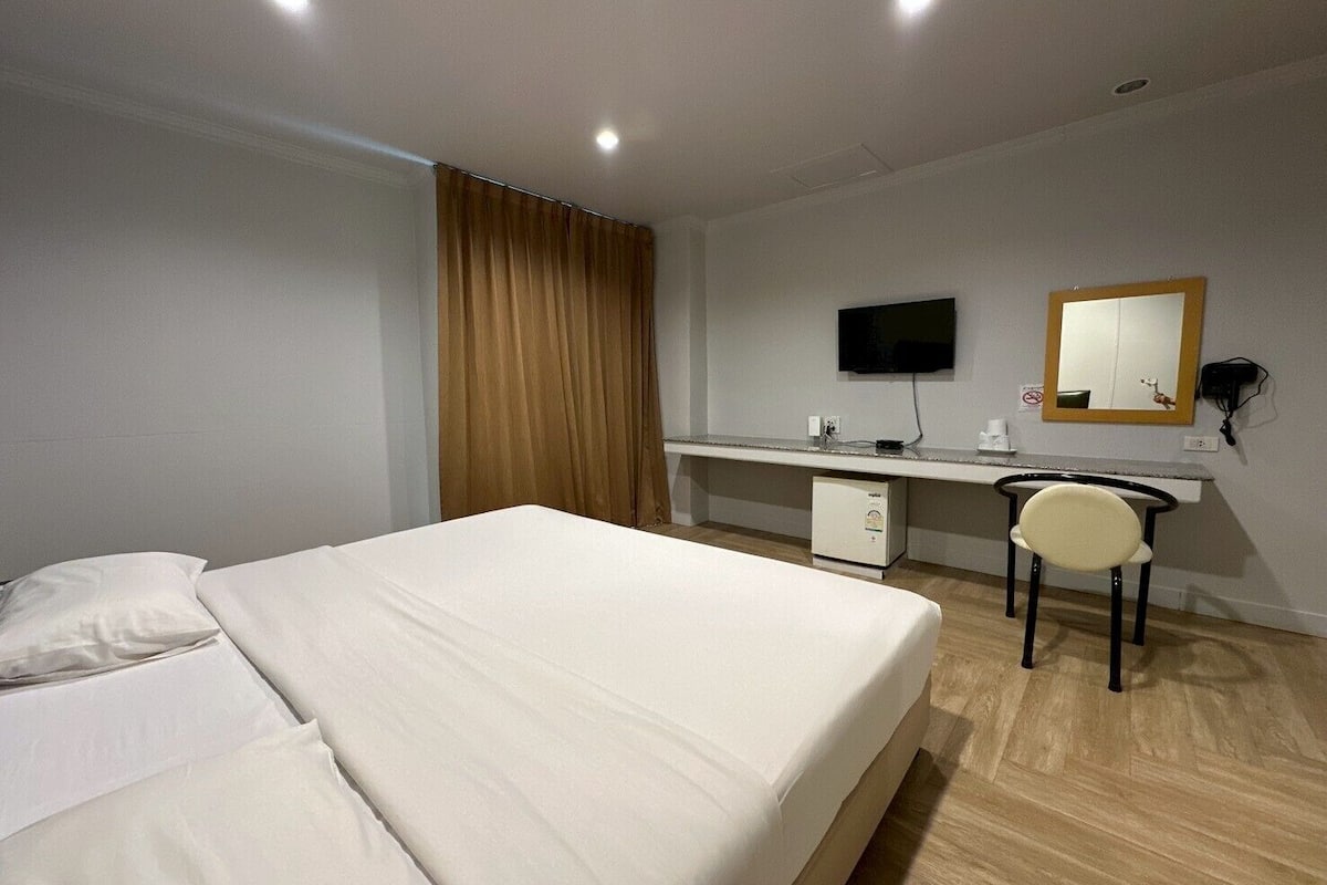 A hotel room with a bed, a desk, a chair, a television, and a mirror.