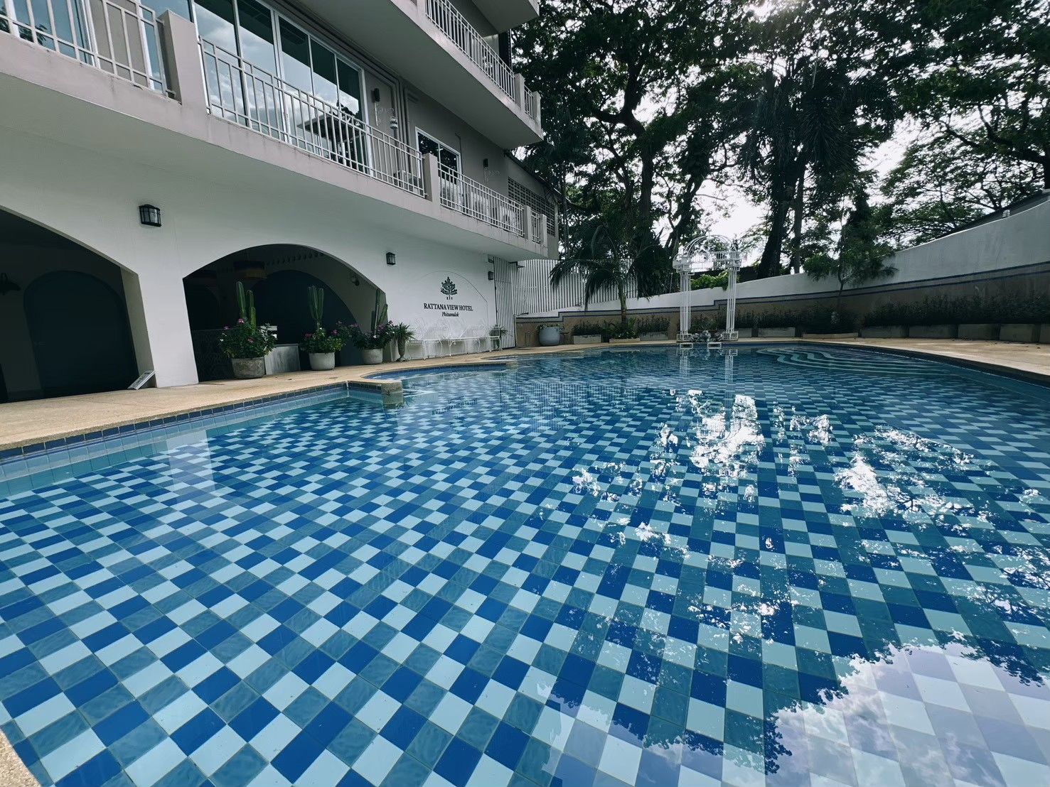 Una piscina con diseño a cuadros, rodeada por un edificio con balcones y un letrero que dice 'Rattanview Hotel'.