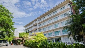 Un hotel de varios pisos con balcones, entrada cubierta y abundante vegetación.