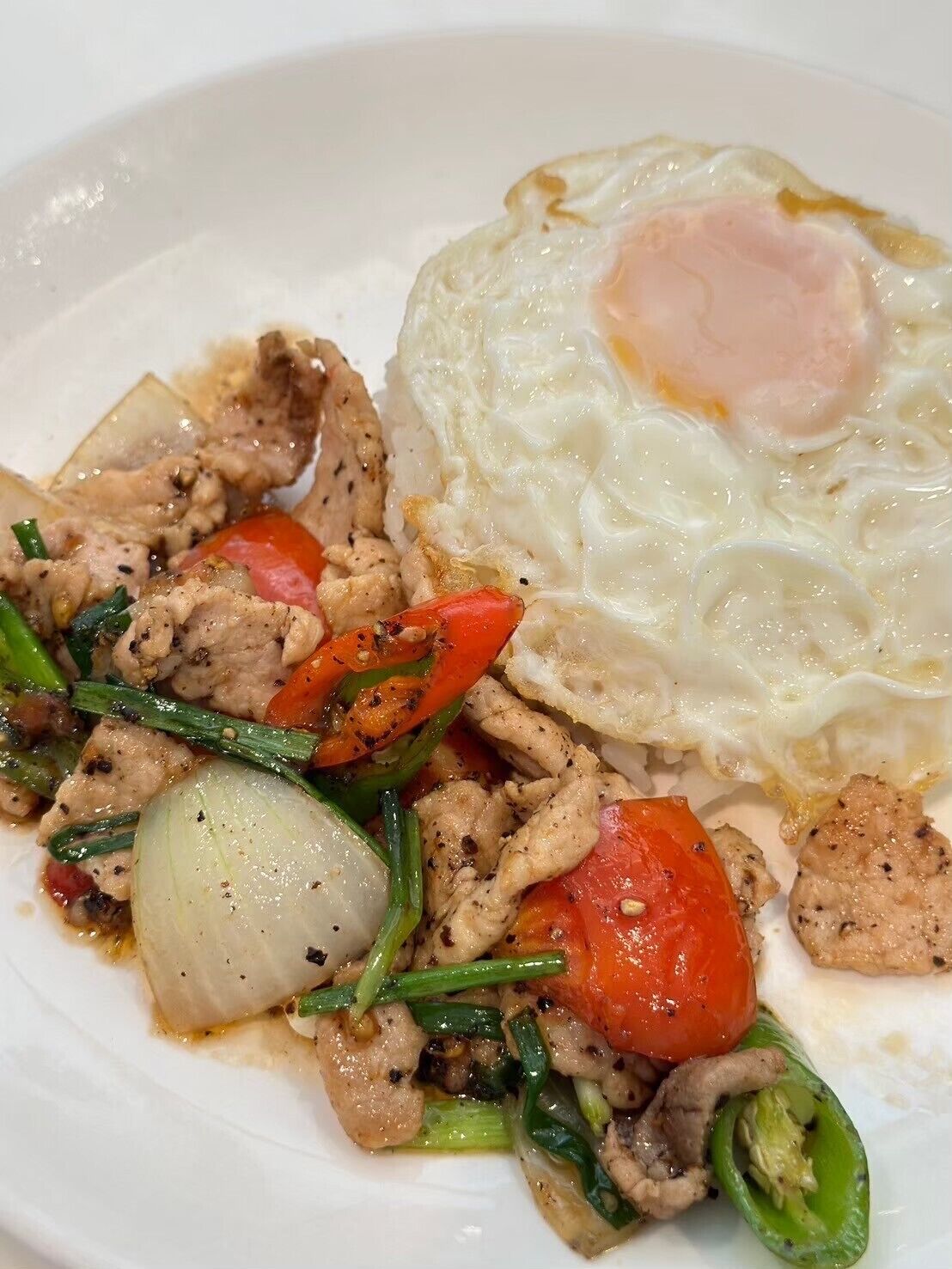 A plate of stir-fried meat with vegetables and a fried egg.