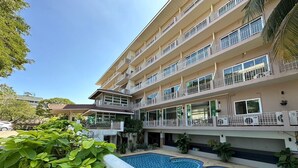 Un hotel de varios pisos con balcones, piscina y abundante vegetación.