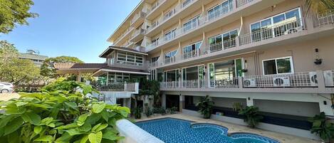 A multi-story hotel with balconies, a swimming pool, and lush greenery.