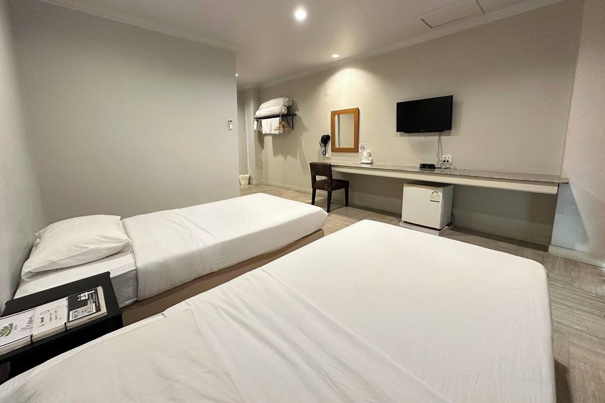 A hotel room with two beds, a desk, a chair, a television, and a small refrigerator.