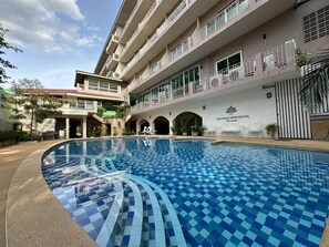 A hotel with a swimming pool, multiple balconies, and a sign indicating the hotel name.