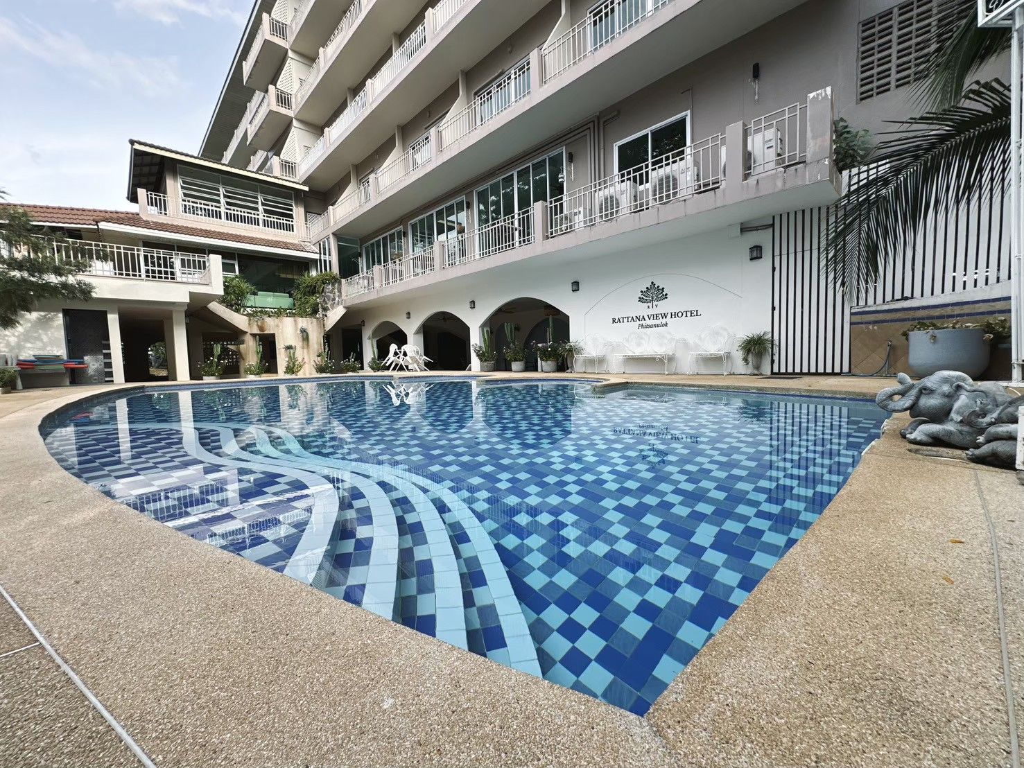 Un hotel con piscina, varios balcones y un cartel con el nombre del hotel.