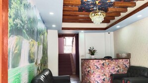 A reception area with a wooden ceiling, a chandelier, a reception desk, and a seating area with black leather sofas and a small yellow stool. - Charming Durbar Hotel  (Kathmandu)
