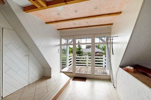 Une pièce avec un plafond en pente, de grandes fenêtres et une terrasse en bois à l’extérieur.