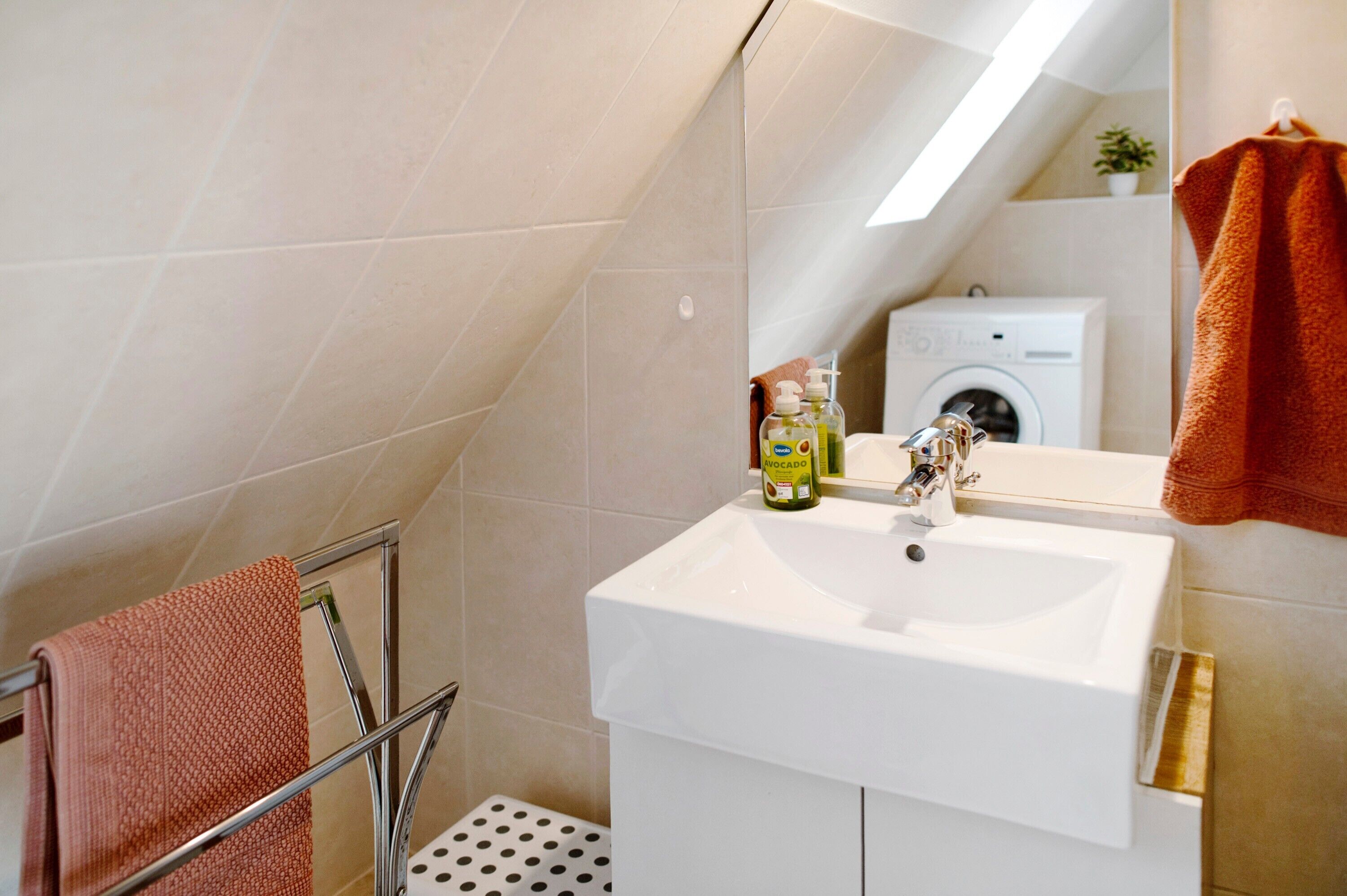 A bathroom with a white sink, a towel rack, a mirror, and a washing machine in the background.