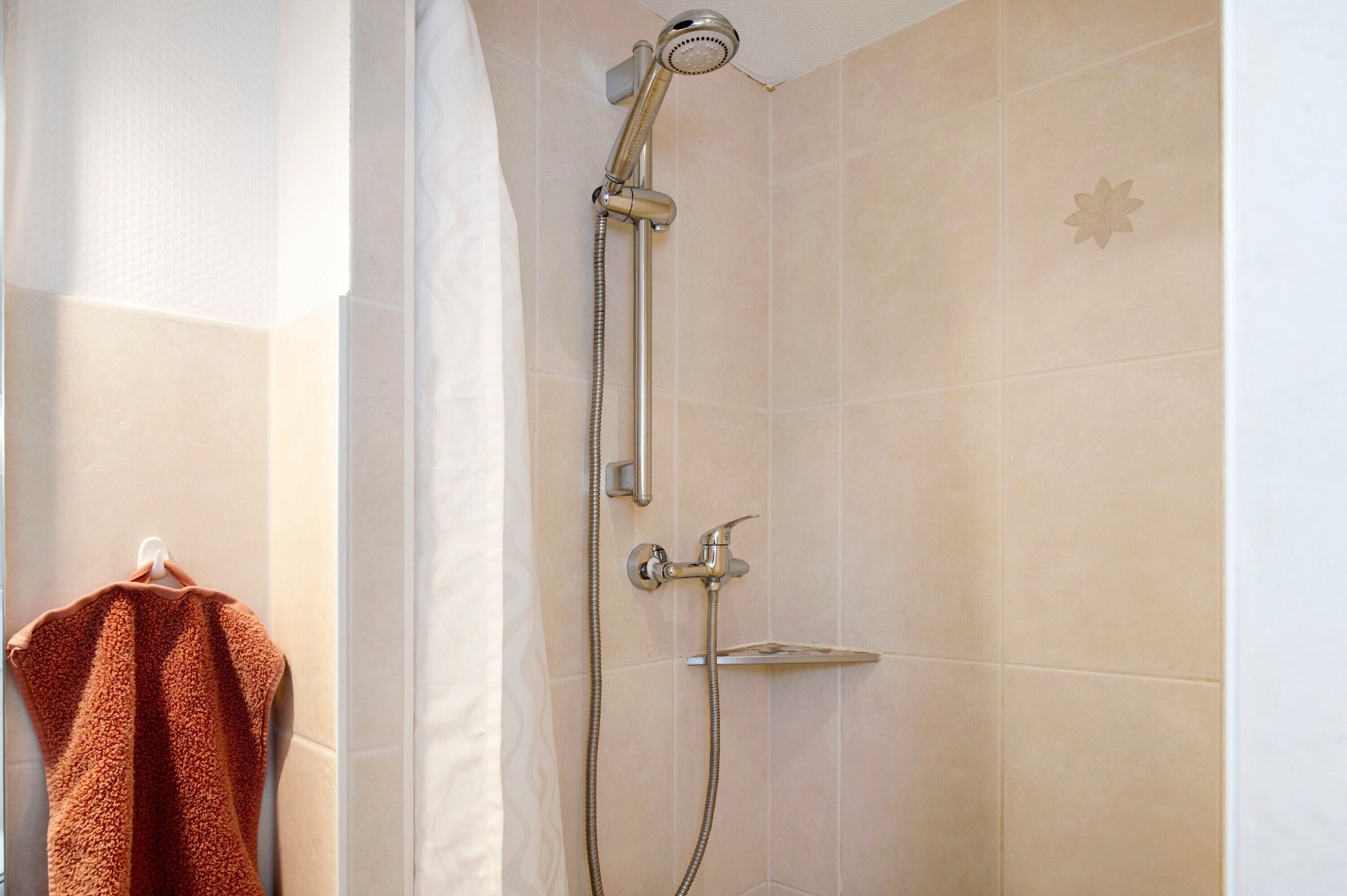 Une douche équipée d’un pommeau de douche à main et d’un robinet fixé au mur.