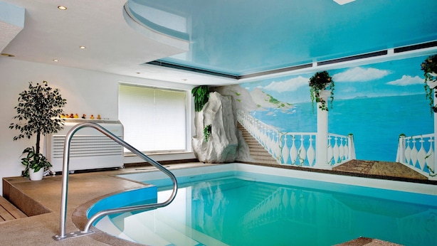 Une piscine dotée d’un toit en verre, d’une balustrade blanche et d’une fresque représentant un paysage côtier.