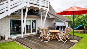 Une terrasse avec des meubles d’extérieur, un barbecue et un toboggan dans le jardin.