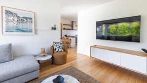Un salon moderne avec un canapé gris, un fauteuil à motifs, une petite table ronde avec une bougie et un grand téléviseur fixé au mur.