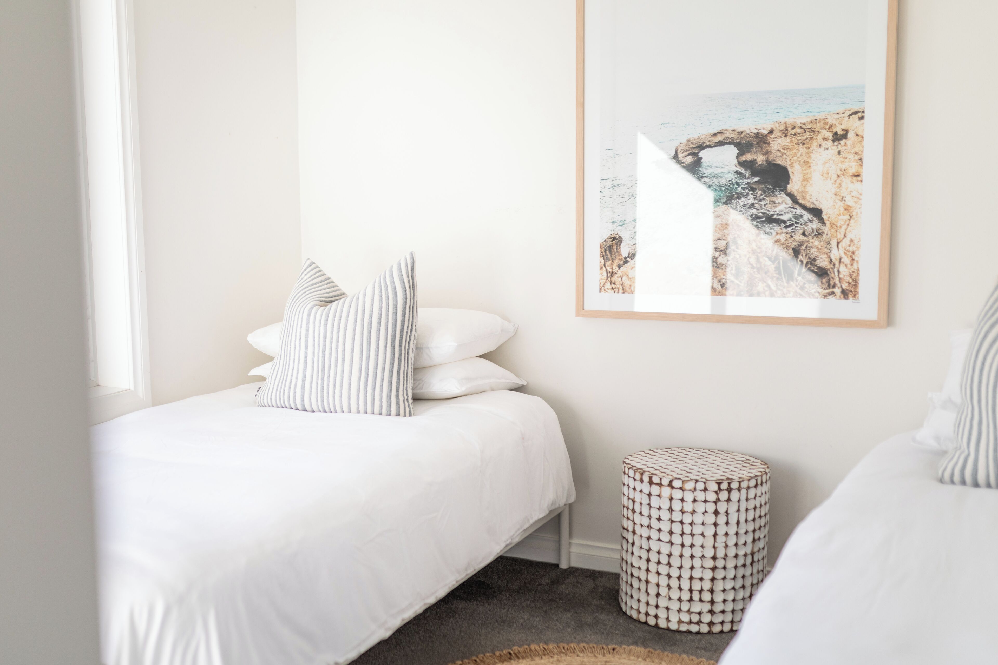 Een slaapkamer met een bed, kussens, een rond poef en een foto in een lijst aan de muur.