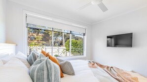 Une chambre dotée d’une grande fenêtre, d’un téléviseur à écran plat fixé au mur et d’un lit agrémenté de plusieurs oreillers et d’une couverture.