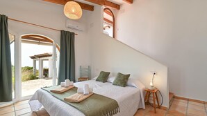 A bedroom with a bed, a bedside table with a lamp, a window with curtains, and a view of the outdoors. - Los Lobitos - Benitachell, Costa Blanca (Benitachell)