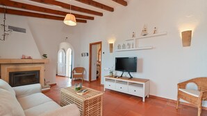 A living room with a fireplace, a television, and a wicker chair. - Los Lobitos - Benitachell, Costa Blanca (Benitachell)