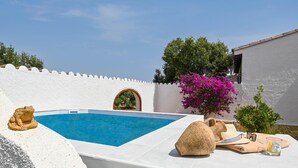 A pool area with a white wall, a stone frog sculpture, and a small table with a towel and sunglasses. - Los Lobitos - Benitachell, Costa Blanca (Benitachell)