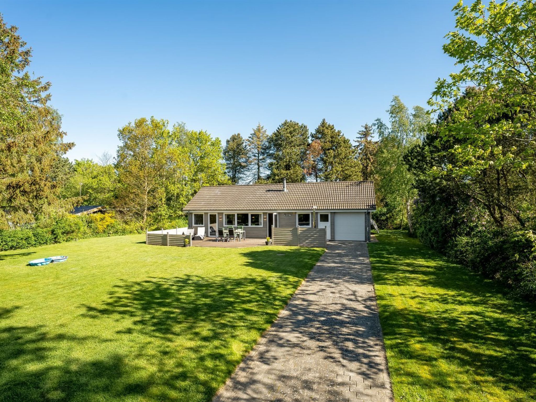 A single-story house with a paved driveway leading to a front door, surrounded by a well-maintained lawn and trees.