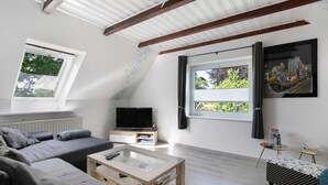 A modern living room with a sofa, TV, coffee table, and two small side tables. - Apartment 'De Lütte Moehl' with Natural Swimming Pond and Shared Terrace (Hollingstedt)
