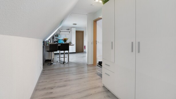 A modern kitchen with white cabinets, a dining area with a black chair, and a wooden floor. - Apartment 'De Lütte Moehl' with Natural Swimming Pond and Shared Terrace (Hollingstedt)
