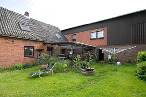 Un jardin à l’arrière d’une maison, avec une pelouse, un fil à linge et un fauteuil de jardin.
