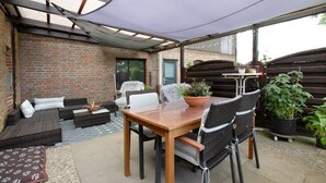 A patio with a wooden table and wicker chairs, a brick wall, and a covered area with a table and chairs. - Apartment 'De Lütte Moehl' with Natural Swimming Pond and Shared Terrace (Hollingstedt)