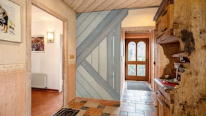 Un couloir avec un escalier en bois, un radiateur et une porte donnant sur l’extérieur.