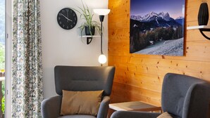 A room with a wooden wall, a clock, a plant, a lamp, and a framed picture.
