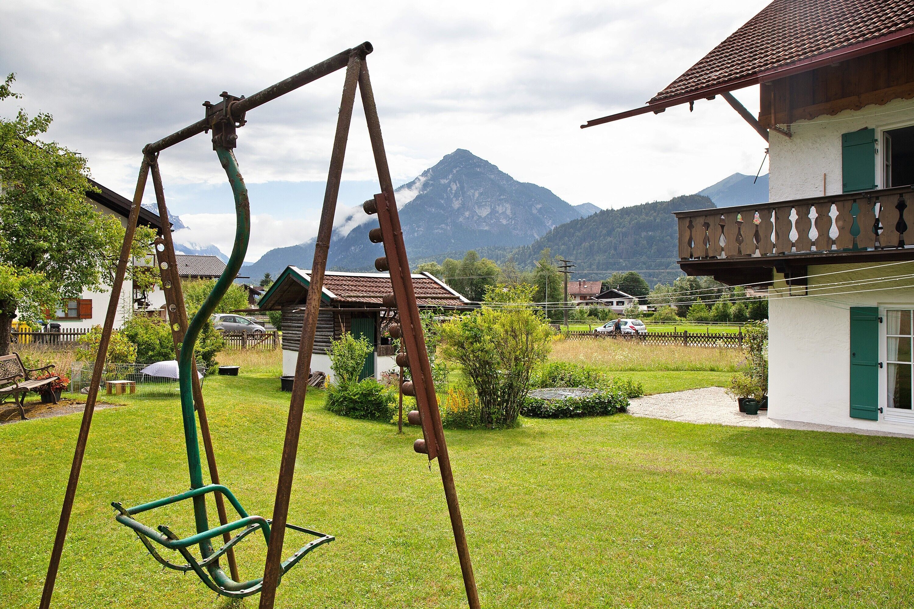 A residential area with a swing set, a house with a balcony, and a mountain in the background.
