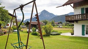 A residential area with a swing set, a house with a balcony, and a mountain in the background.