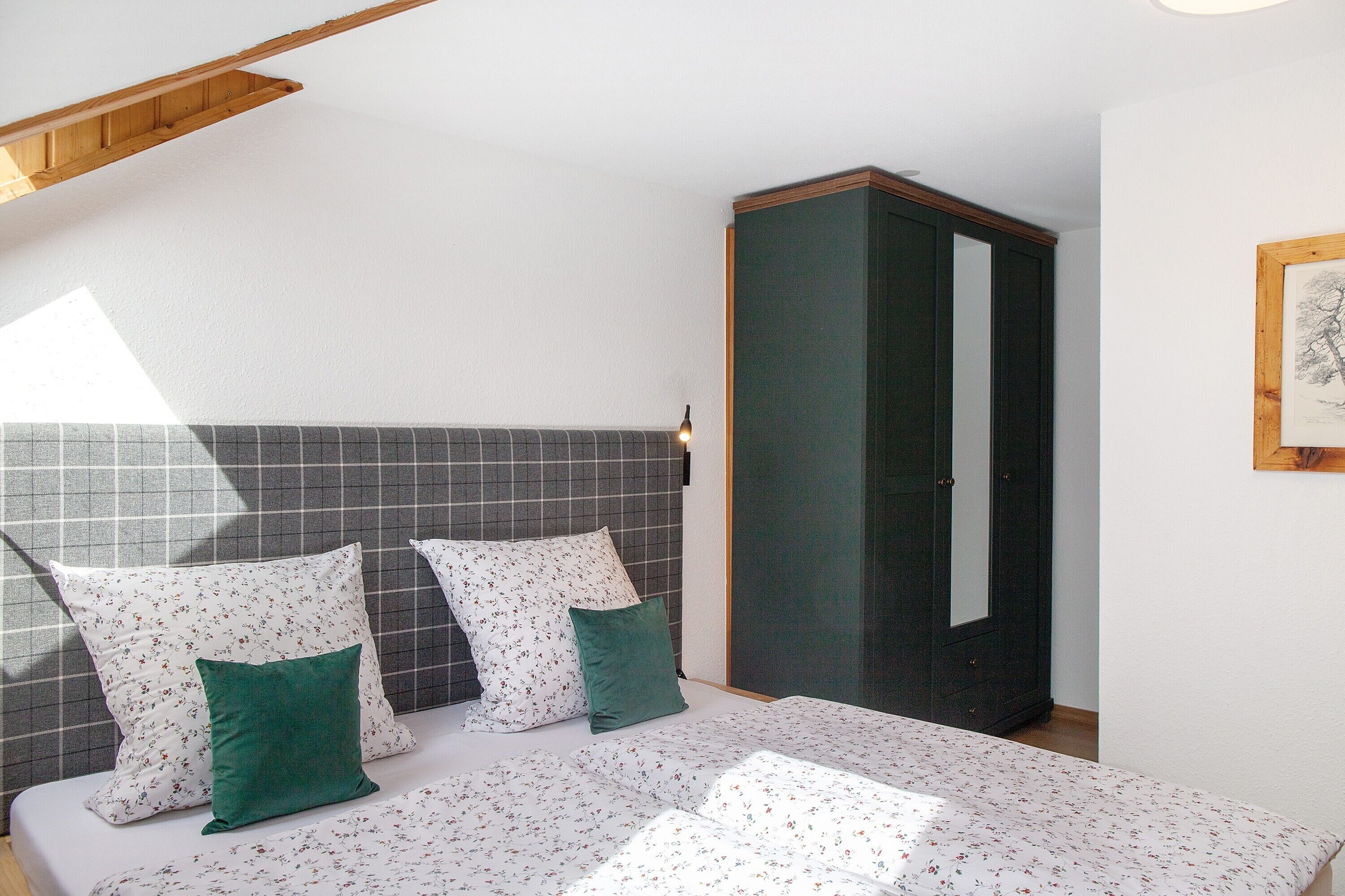 A bedroom with a bed, pillows, a wardrobe, and a framed picture on the wall.