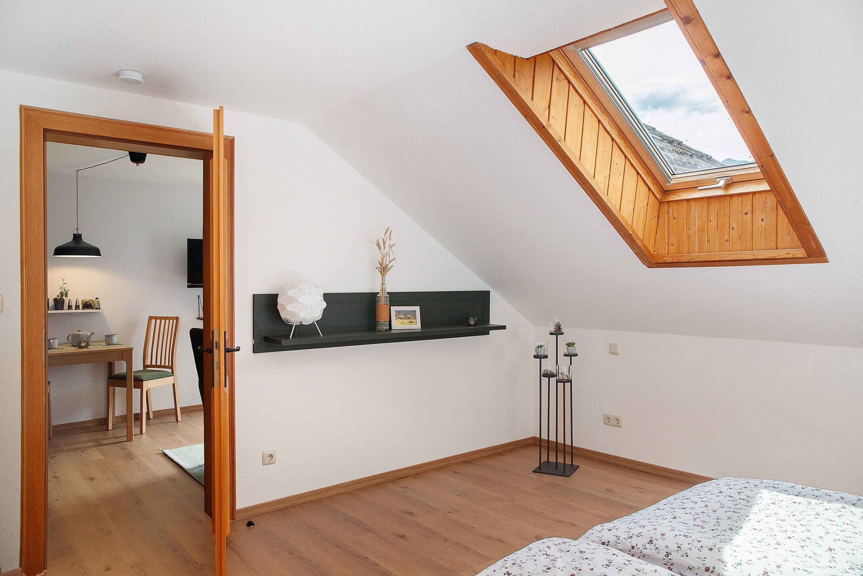 A room with a sloped ceiling, a skylight, a desk, a chair, a bed, and a small plant.